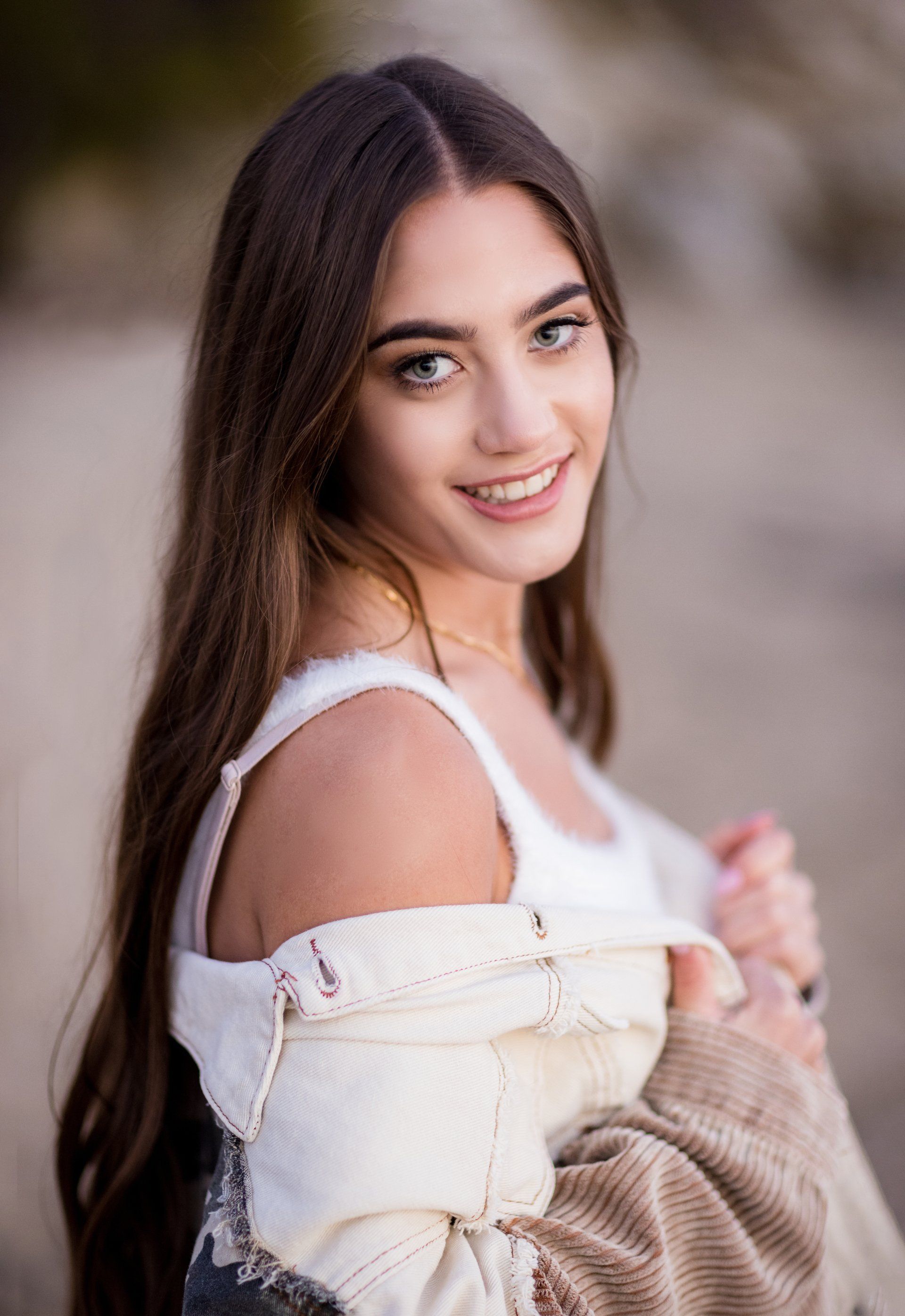 A young woman with long hair is wearing a white tank top and a brown jacket.
