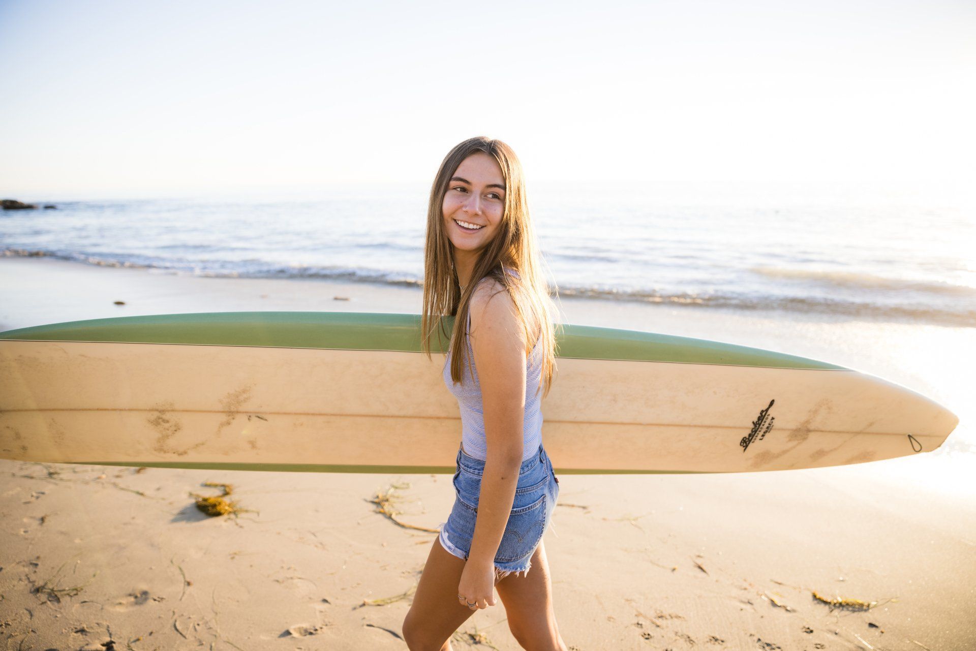 A woman is walking on the beach with a surfboard.