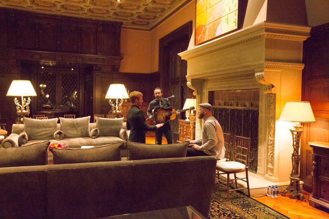 A man is playing a guitar in a living room while a woman sits on a couch.