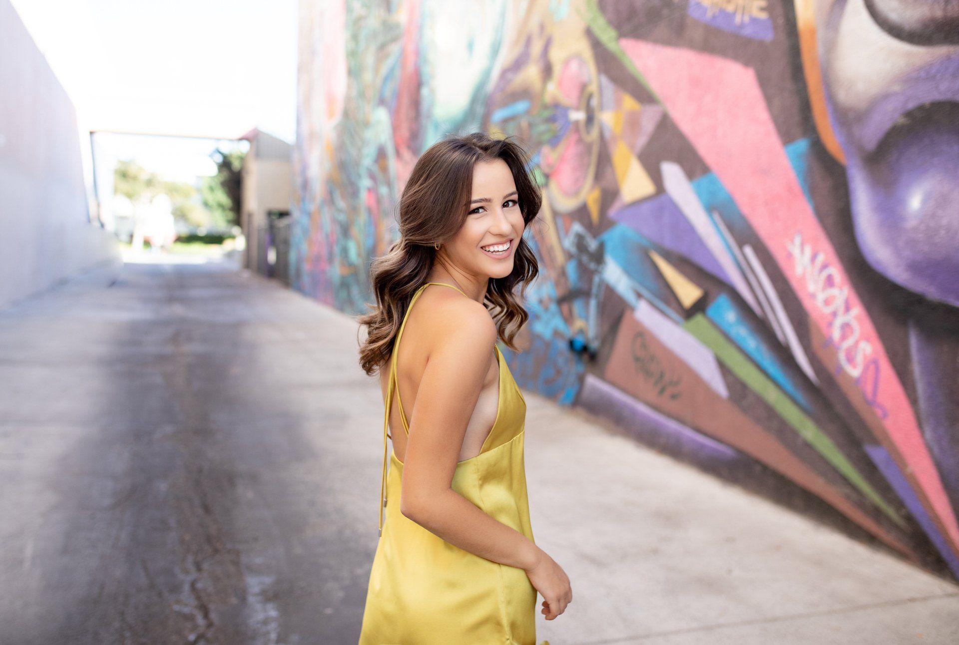 A woman in a yellow dress is standing in front of a graffiti wall.