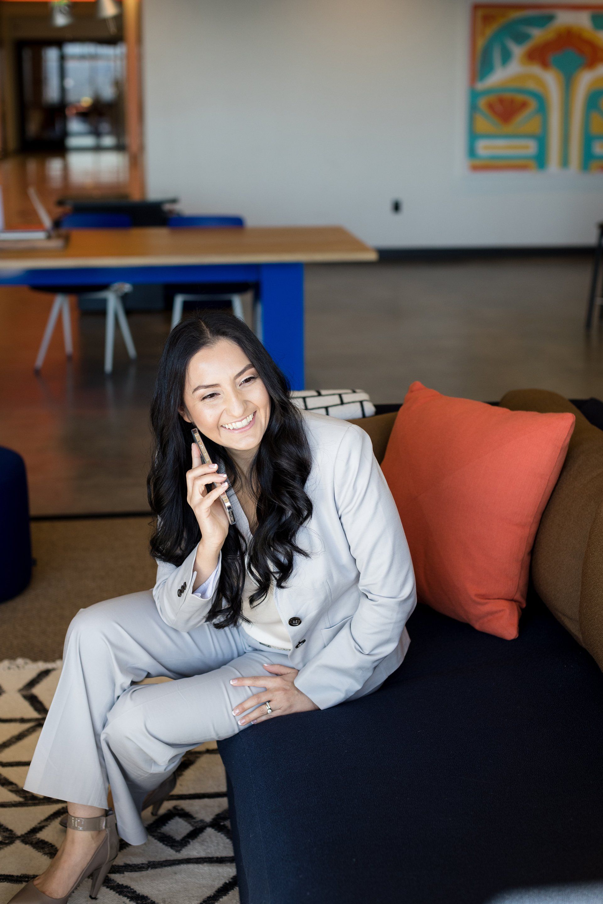 A woman in a suit is sitting on a couch talking on a cell phone.