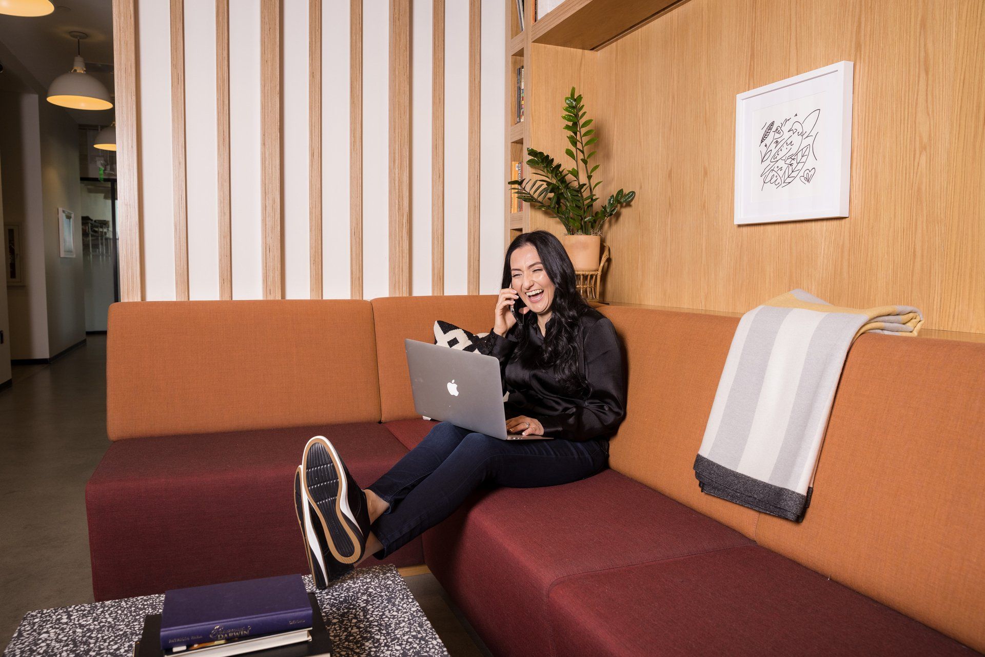 A woman is sitting on a couch with a laptop and talking on a cell phone.