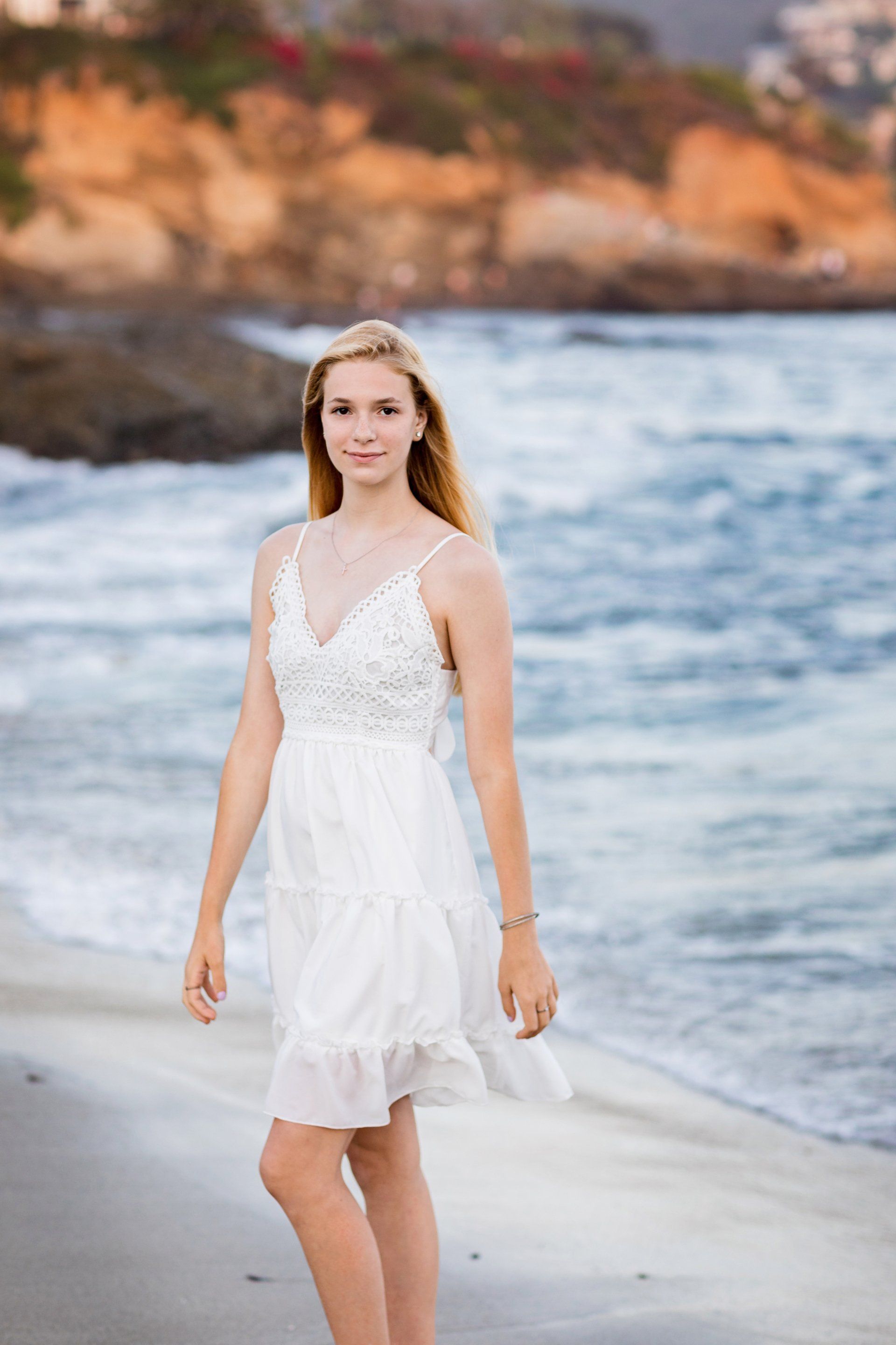 A young woman in a white dress is standing on a beach.