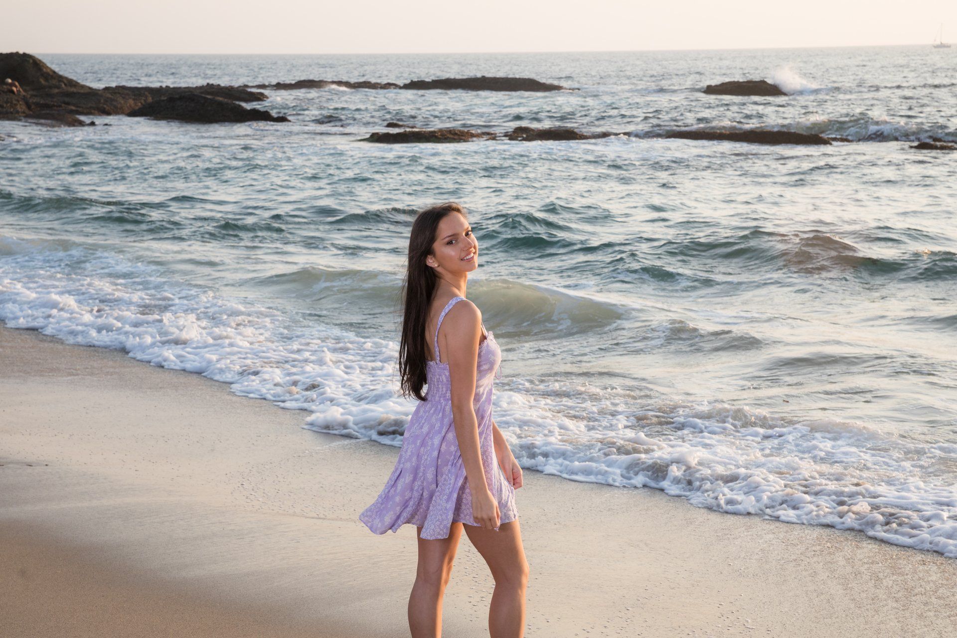 A woman in a dress is standing on a beach near the ocean.