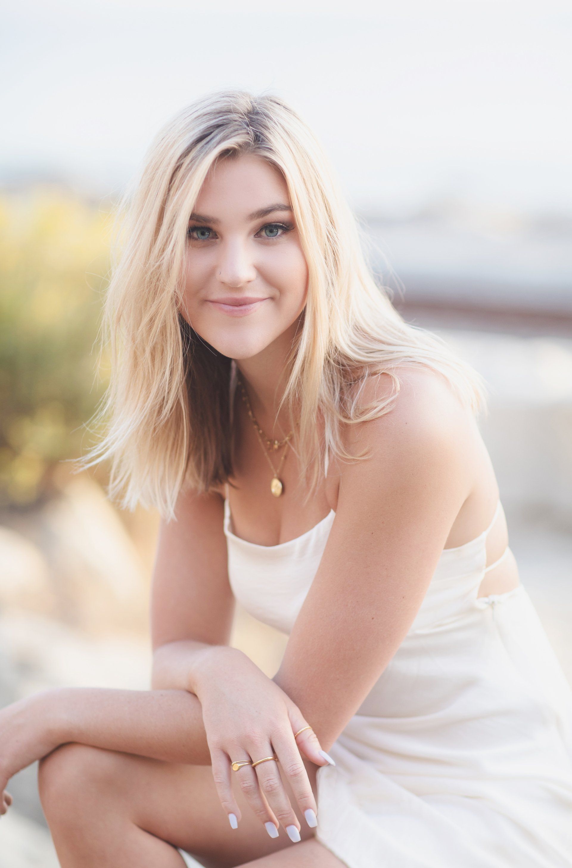 A woman in a white dress is sitting on the ground and smiling.