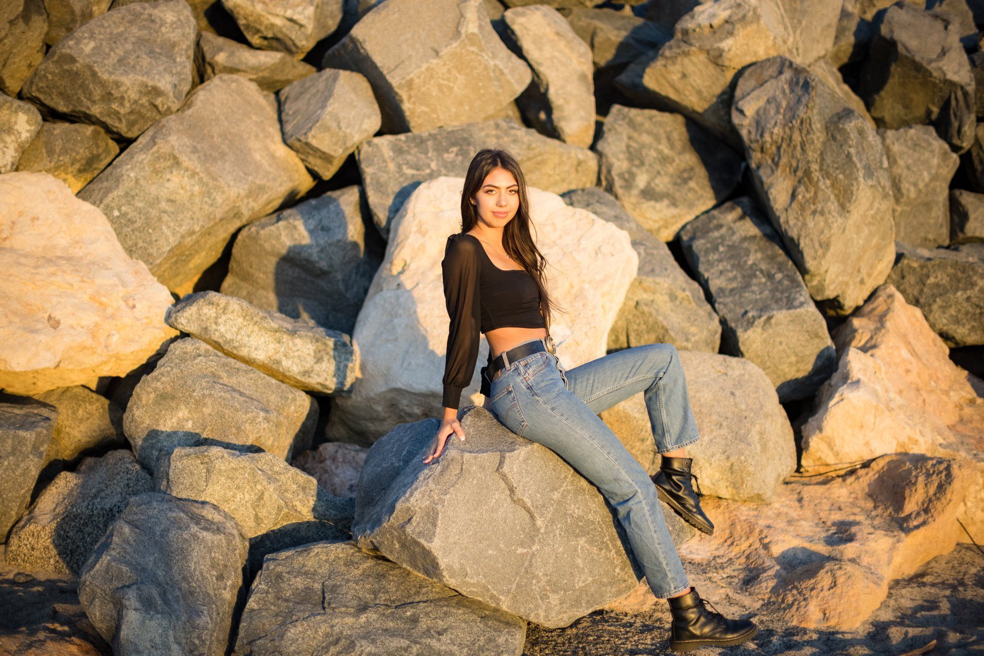 A woman is sitting on a pile of rocks near the ocean.