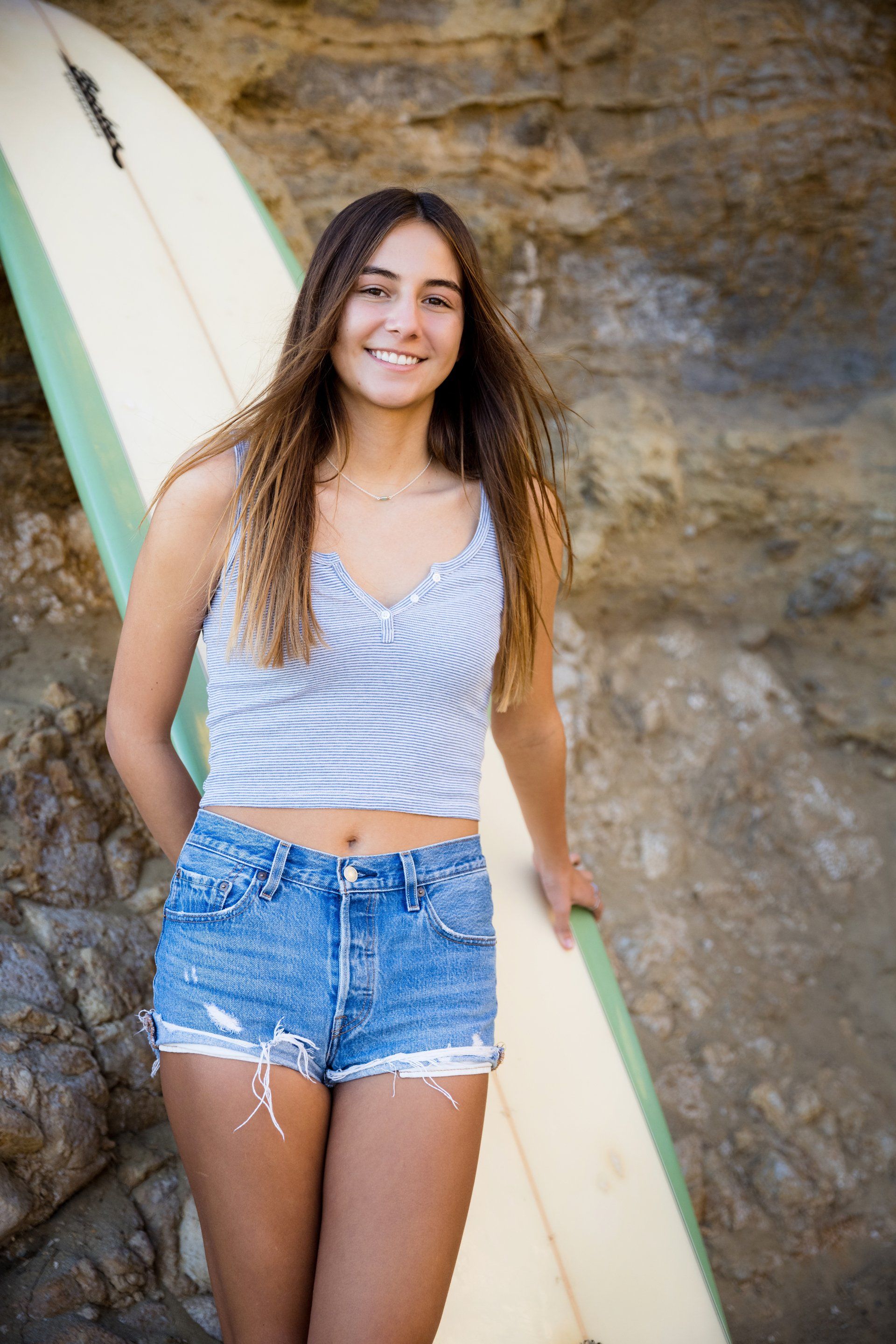 A young woman is standing next to a surfboard on the beach.