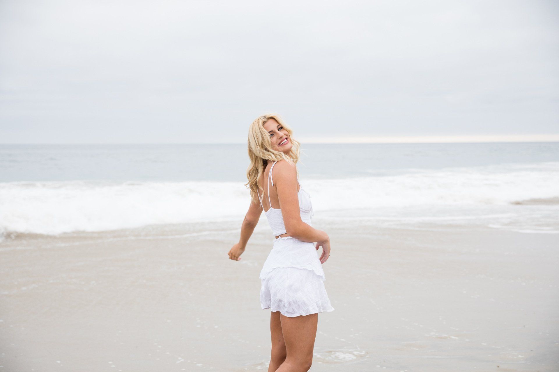 A woman in a white dress is standing on a beach.