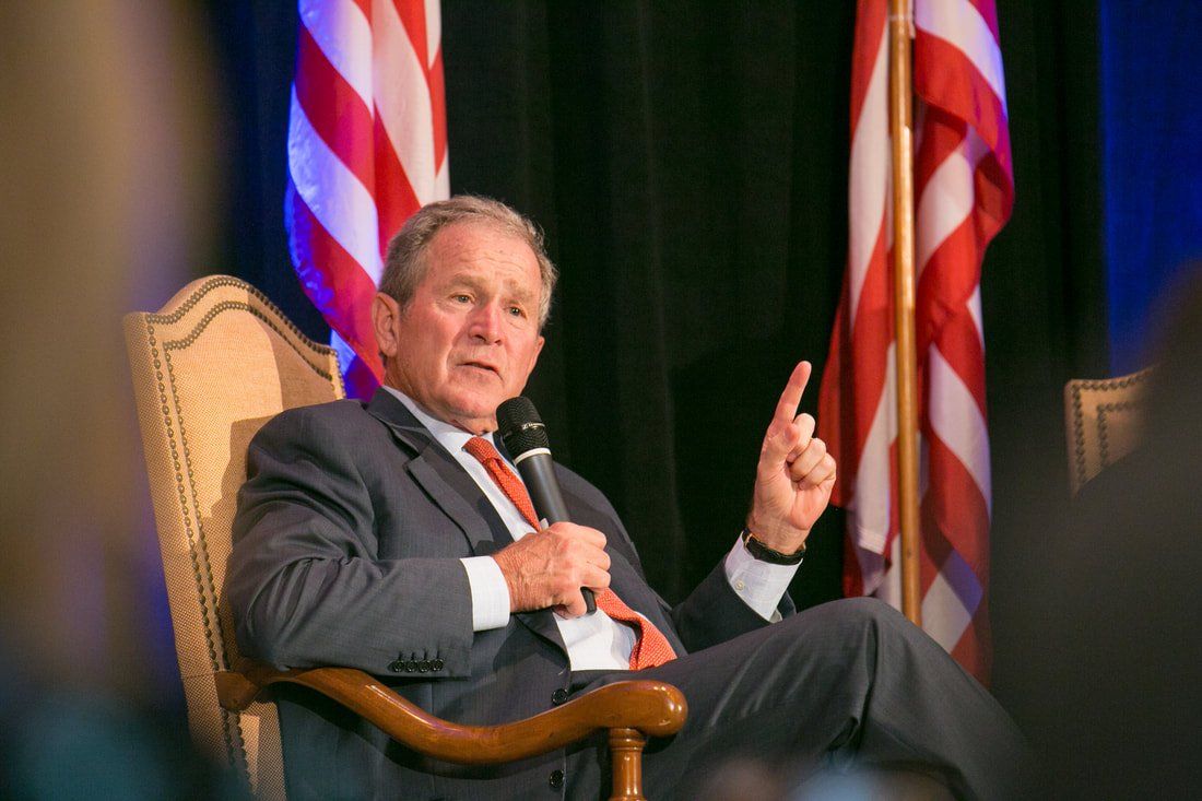 A man in a suit and tie is sitting in a chair talking into a microphone.