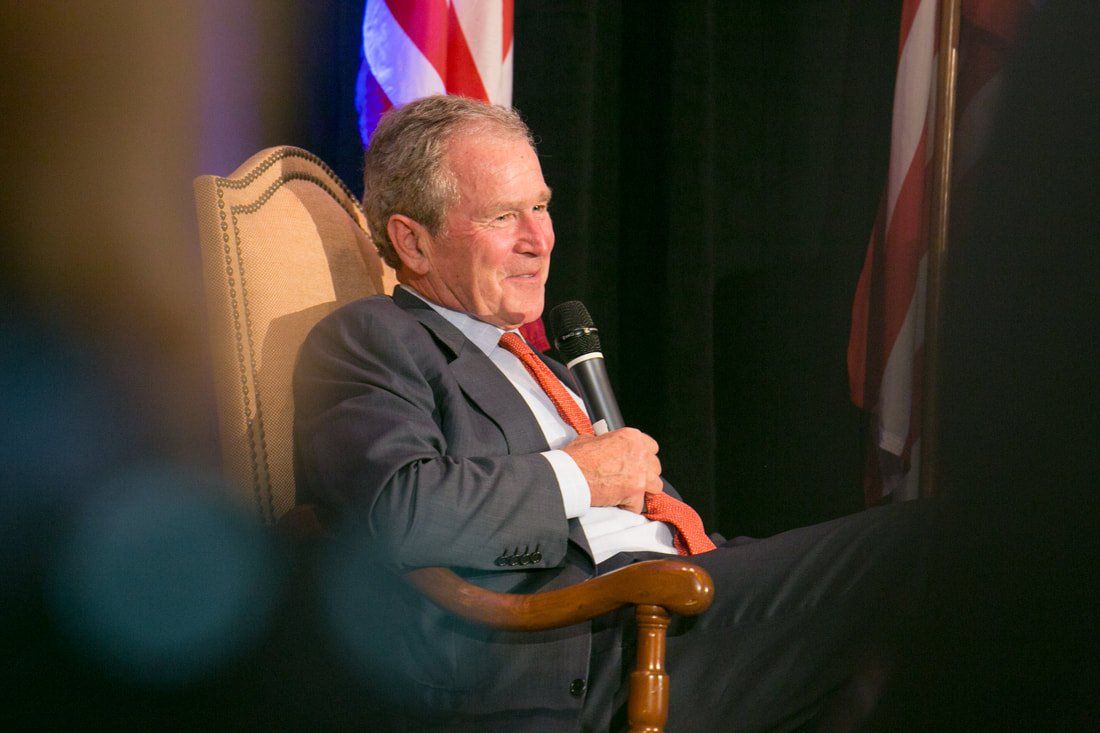 A man in a suit and tie is sitting in a chair holding a microphone.