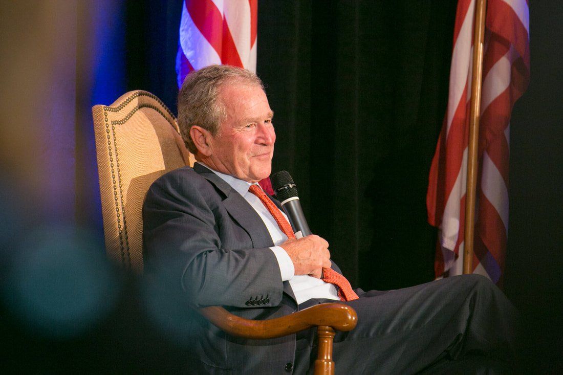 A man in a suit and tie is sitting in a chair holding a microphone.