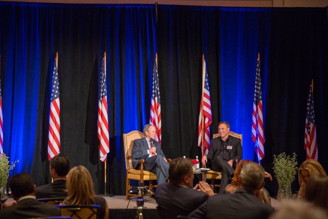 A group of people are sitting in chairs in front of a stage with american flags.