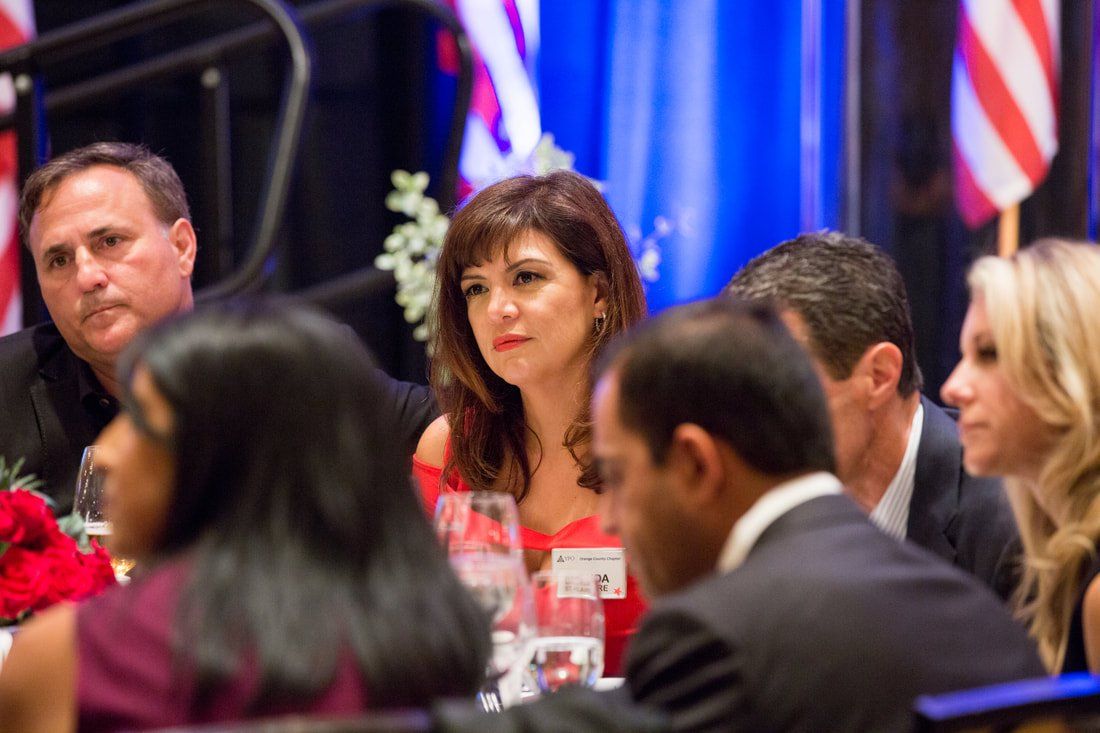 A group of people are sitting at a table with flags in the background.