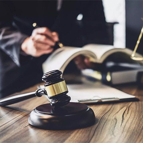 Wooden gavel on a table with a person in the background writing in a book.