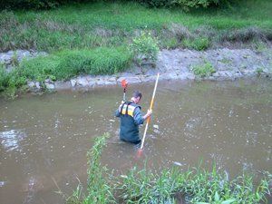 Ein Mann steht in einem Fluss und hält einen Stock.