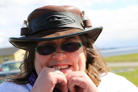 A woman wearing a hat and sunglasses is biting her nails