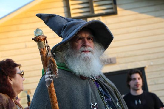 A man with a beard is dressed as a wizard and holding a cane
