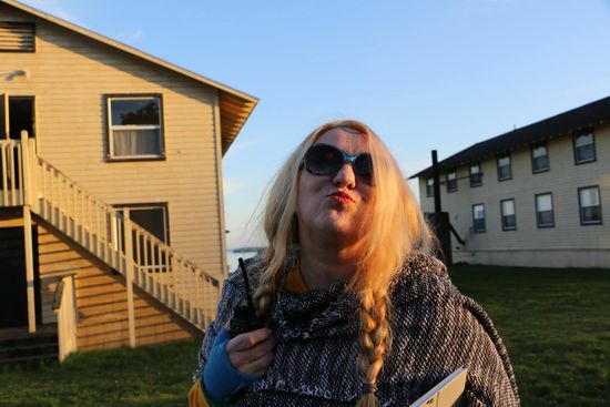 A woman wearing sunglasses is blowing a kiss in front of a building