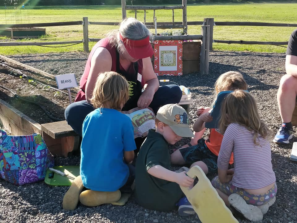 A group of children are sitting on the ground while a woman reads a book to them