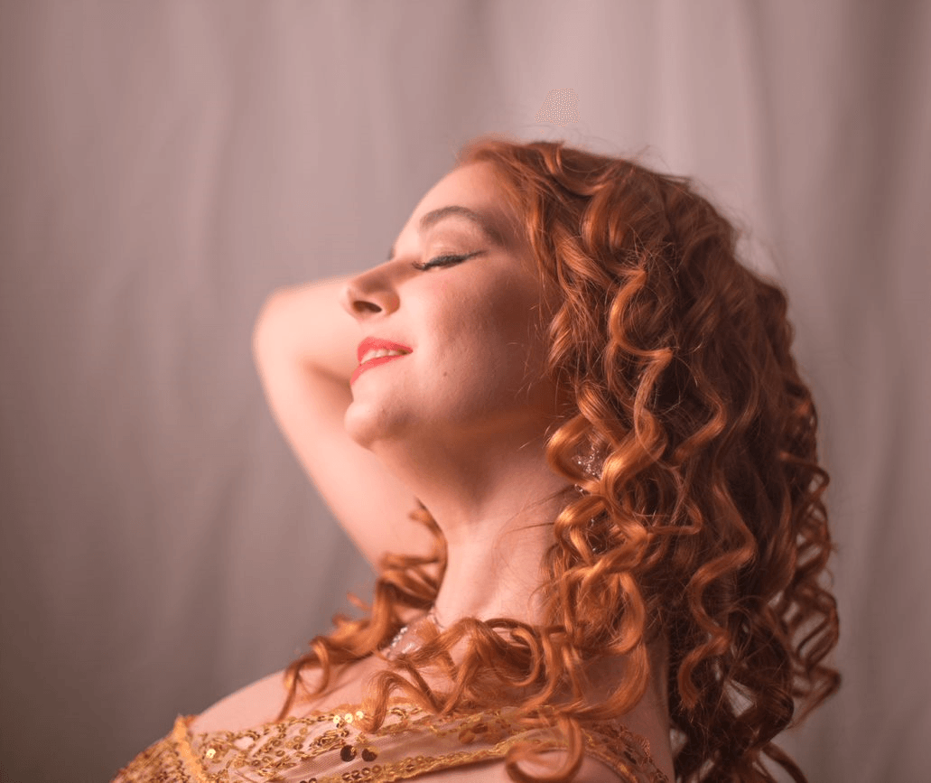 A woman with red curly hair is smiling with her eyes closed, Titania Thunderlily representing Aphrodite
