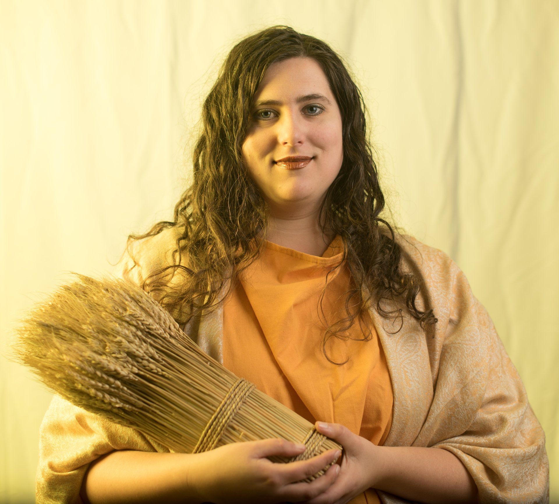 A woman is holding a bunch of wheat in her hands representing Demeter.