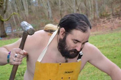 A shirtless man with a beard is holding a hammer, representing Hephaestus.