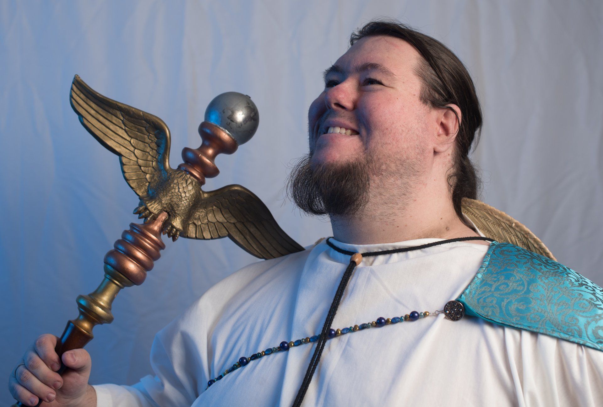 A man with a beard is holding a cane with wings on it, Nikodaemus Shadowsky representing Hermes.