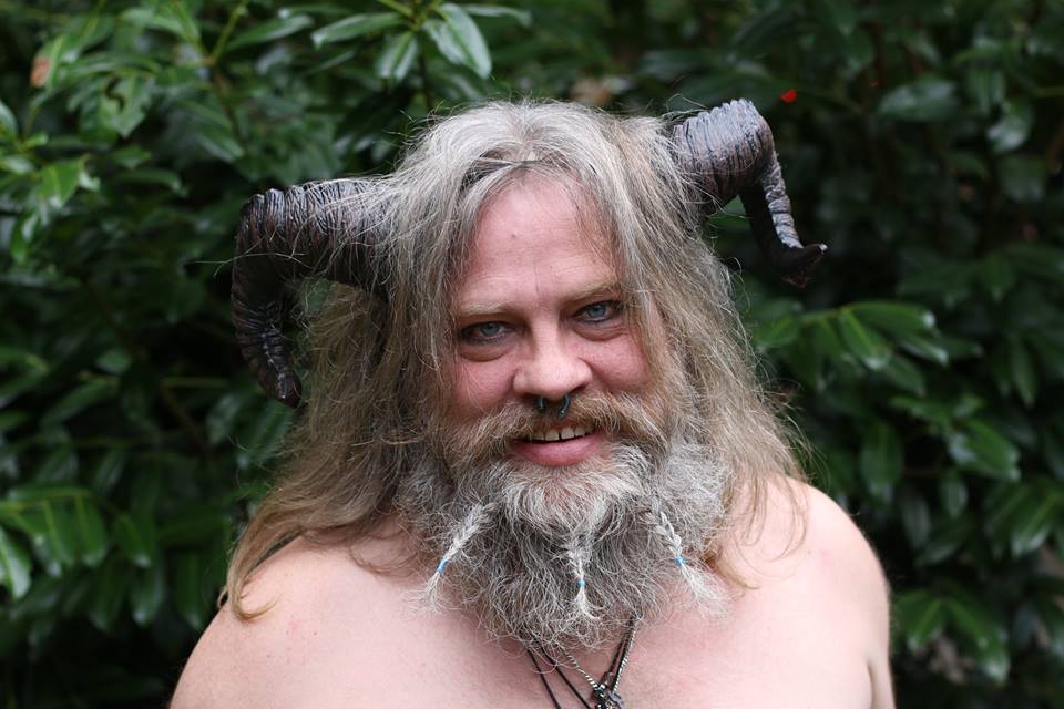 A man with long hair and a beard has horns on his head, representing Pan.