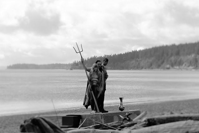 A black and white photo of a man holding a trident on a beach, Poseidon.