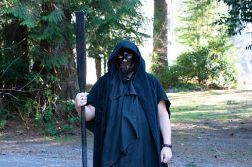 A man in a black cape and mask is holding a pole, representing Hades.