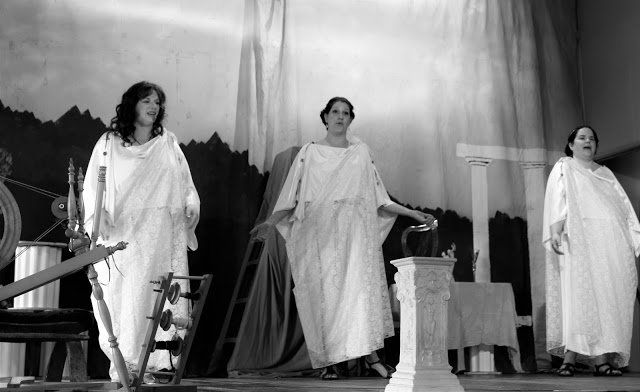 Three women in white robes are standing on a stage., The Graces at Spring Mysteries