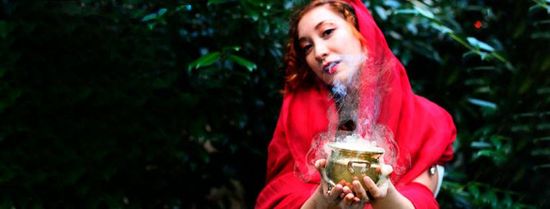 A woman in a red hood is holding a cup in her hands.