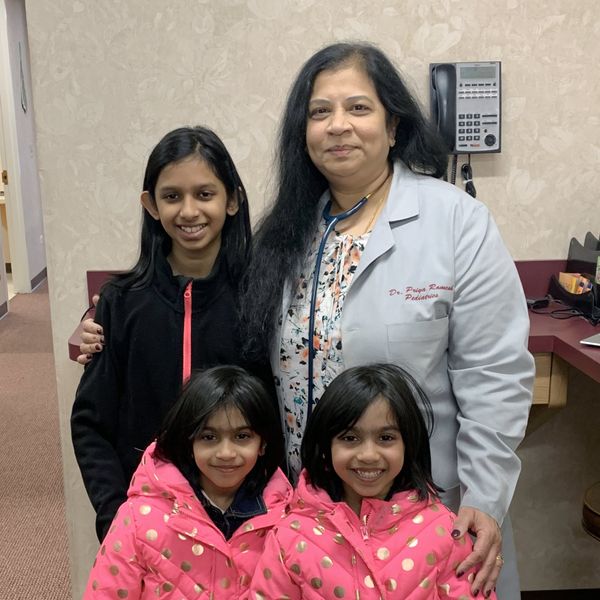 A female doctor with a stethoscope and four smiling girls in a medical office. Dr. Priya Ramesh