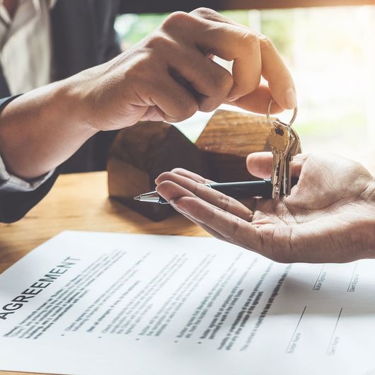 Estate agent giving house keys to customer and sign agreement in office.
