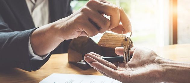 Estate agent giving house keys to customer and sign agreement in office.