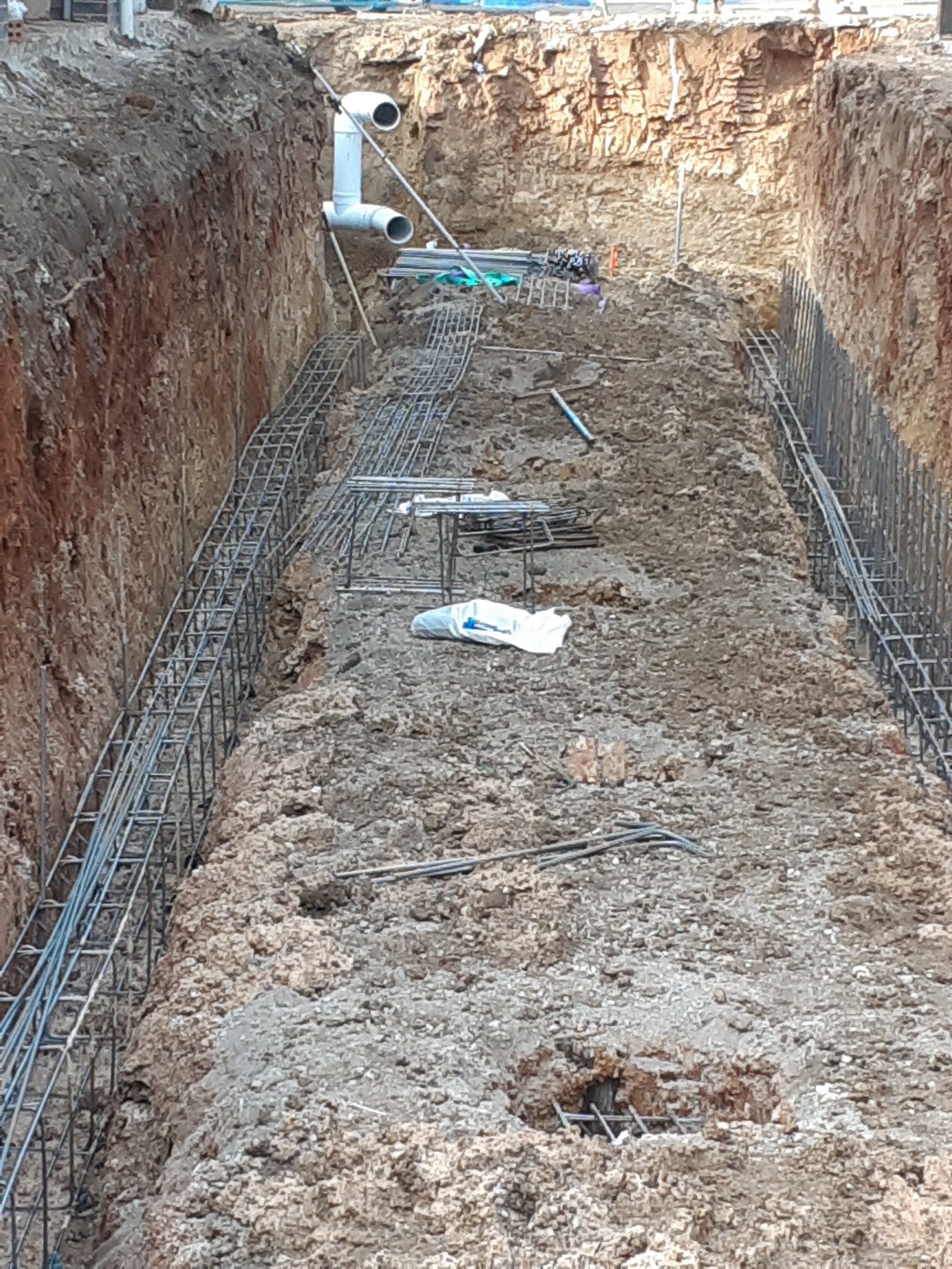 Excavated trench with rebar, pipes, and dirt walls at a construction site