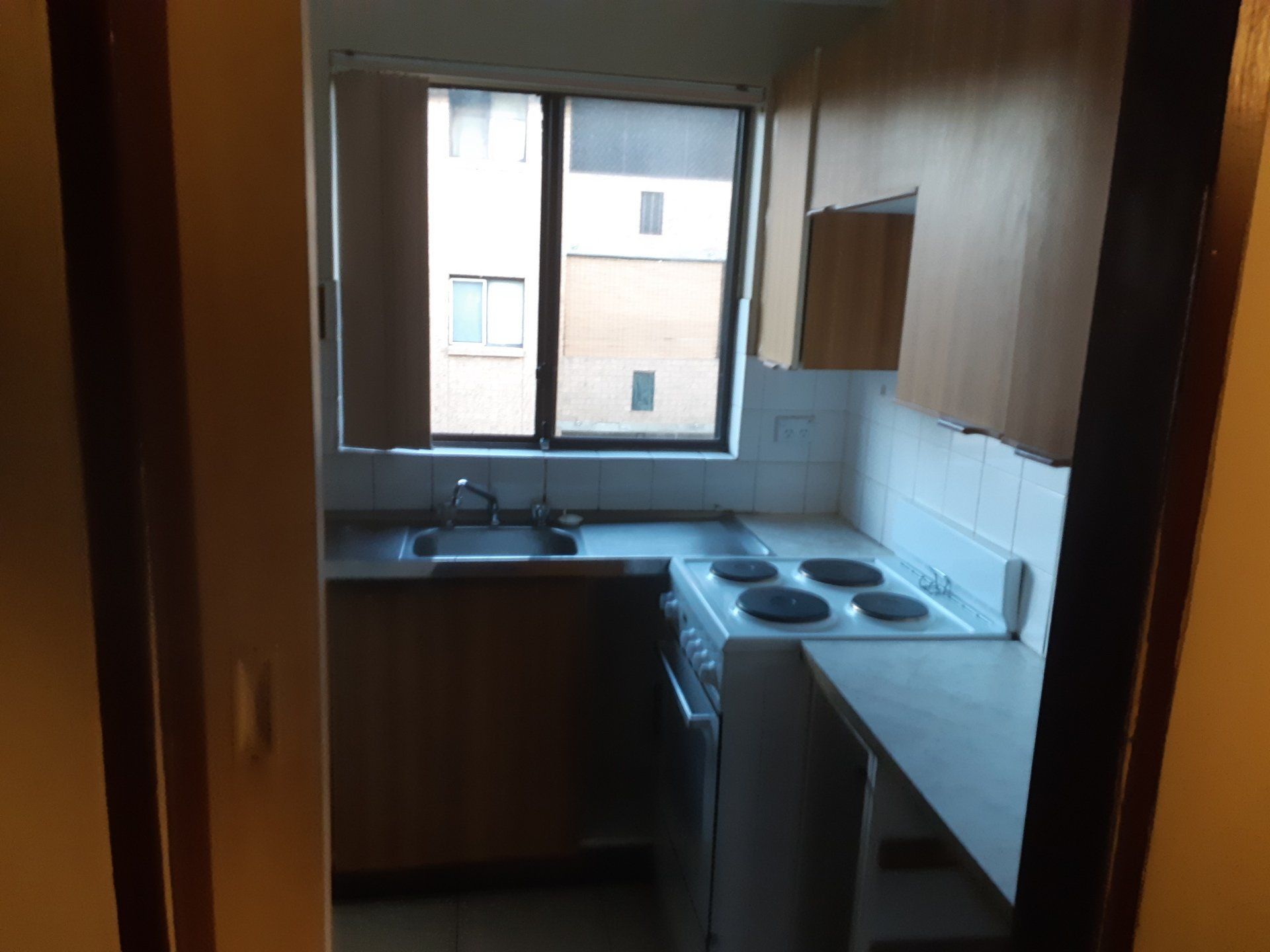 Small kitchen with wooden cabinets, sink by a window, white stove, and gray countertop.