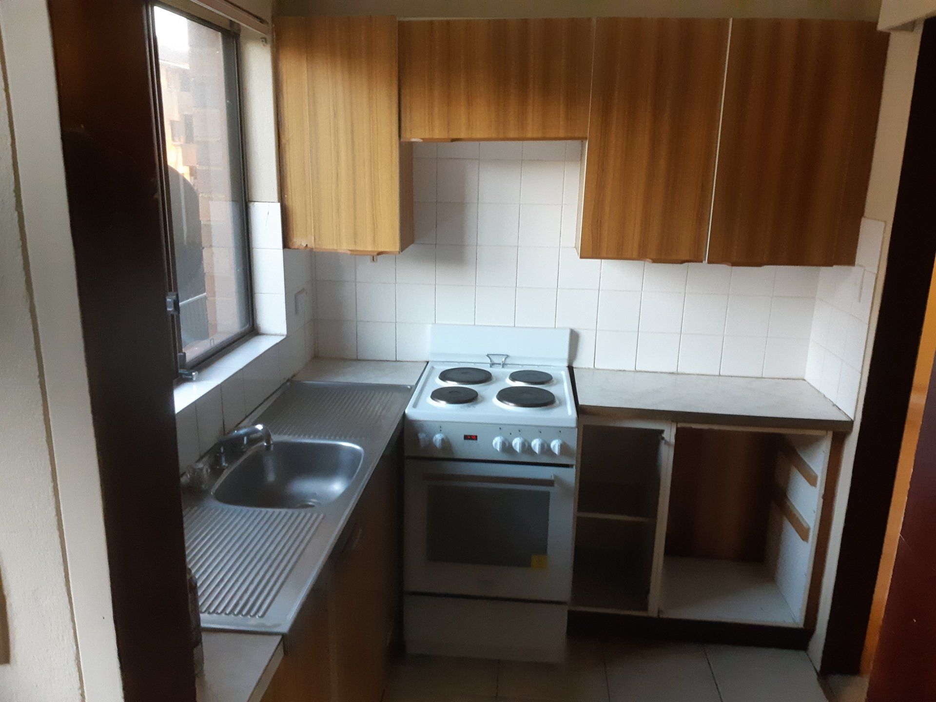 Small kitchen with stove, sink, wooden cabinets, and white tile backsplash.