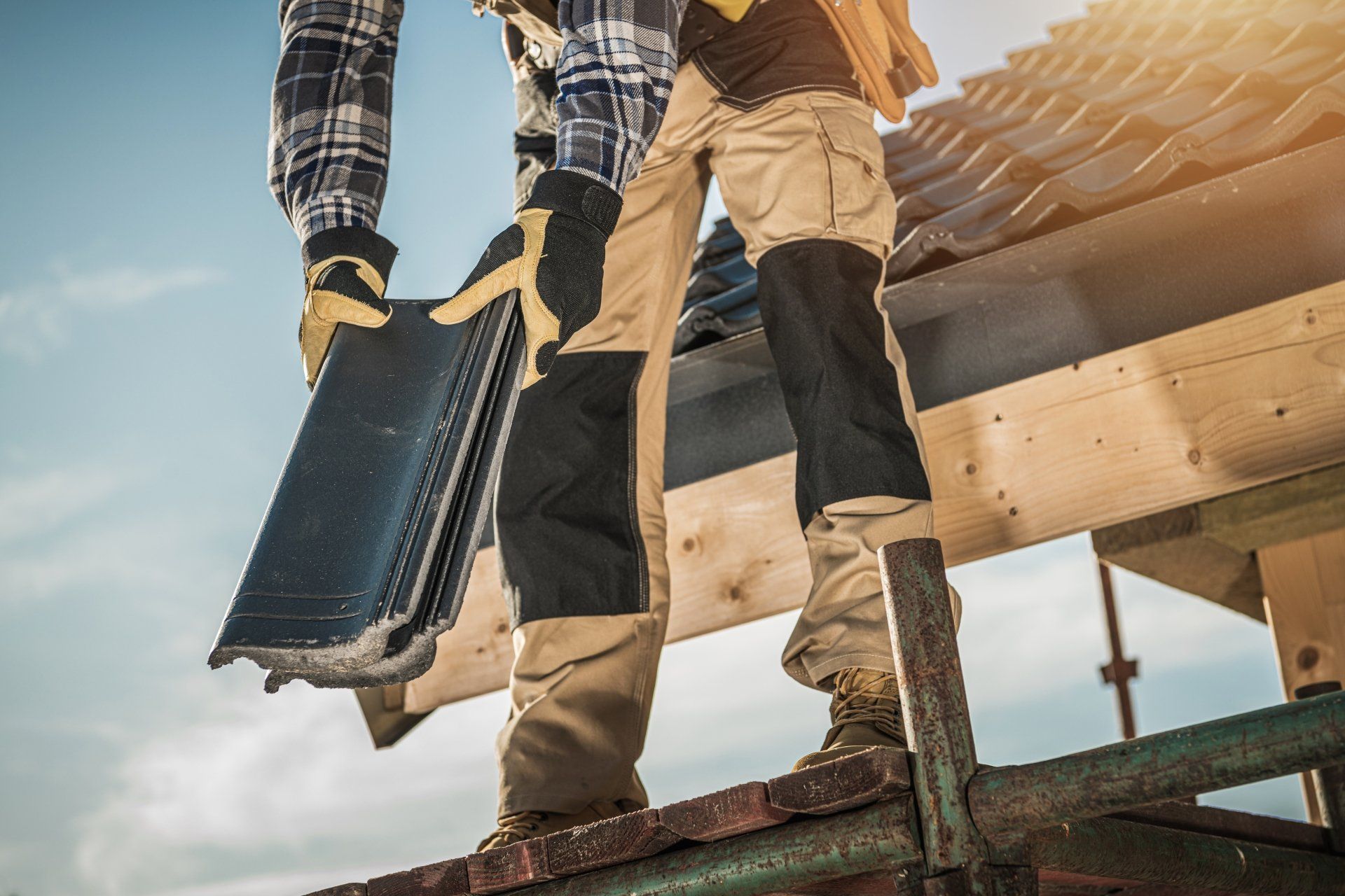 Two workers on a roof carrying tools, with shingles and wood framing visible.
