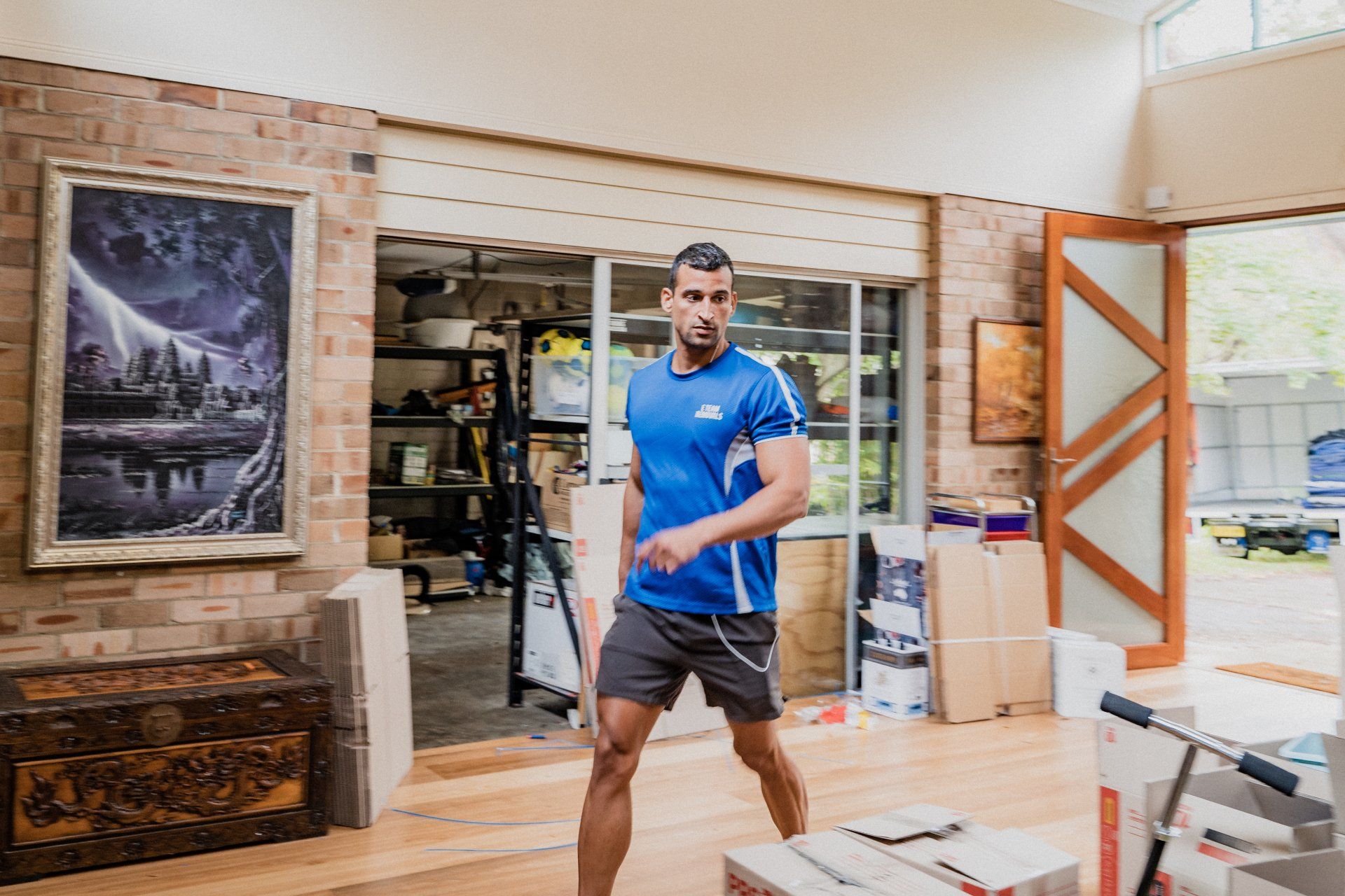 Man standing in a workshop, wearing a blue shirt and gray shorts, with tools and materials around him