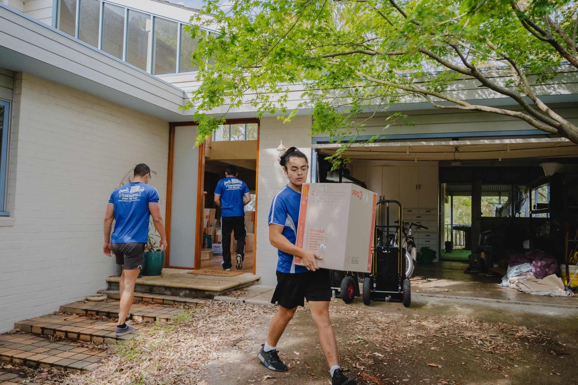 People carrying boxes into a house during a move, with a doorway and garage visible.