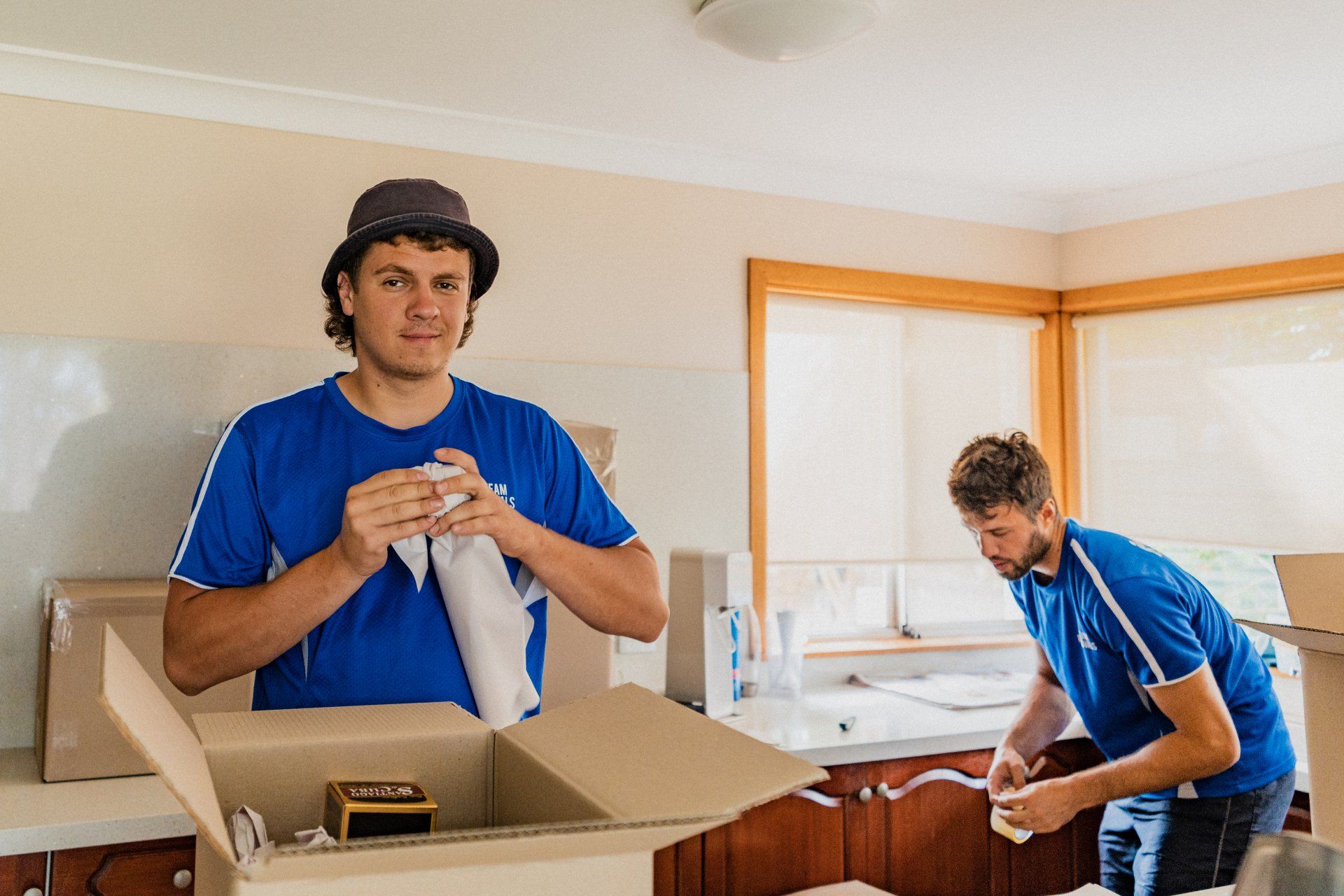 Two movers in blue shirts packing kitchen items in a bright home interior