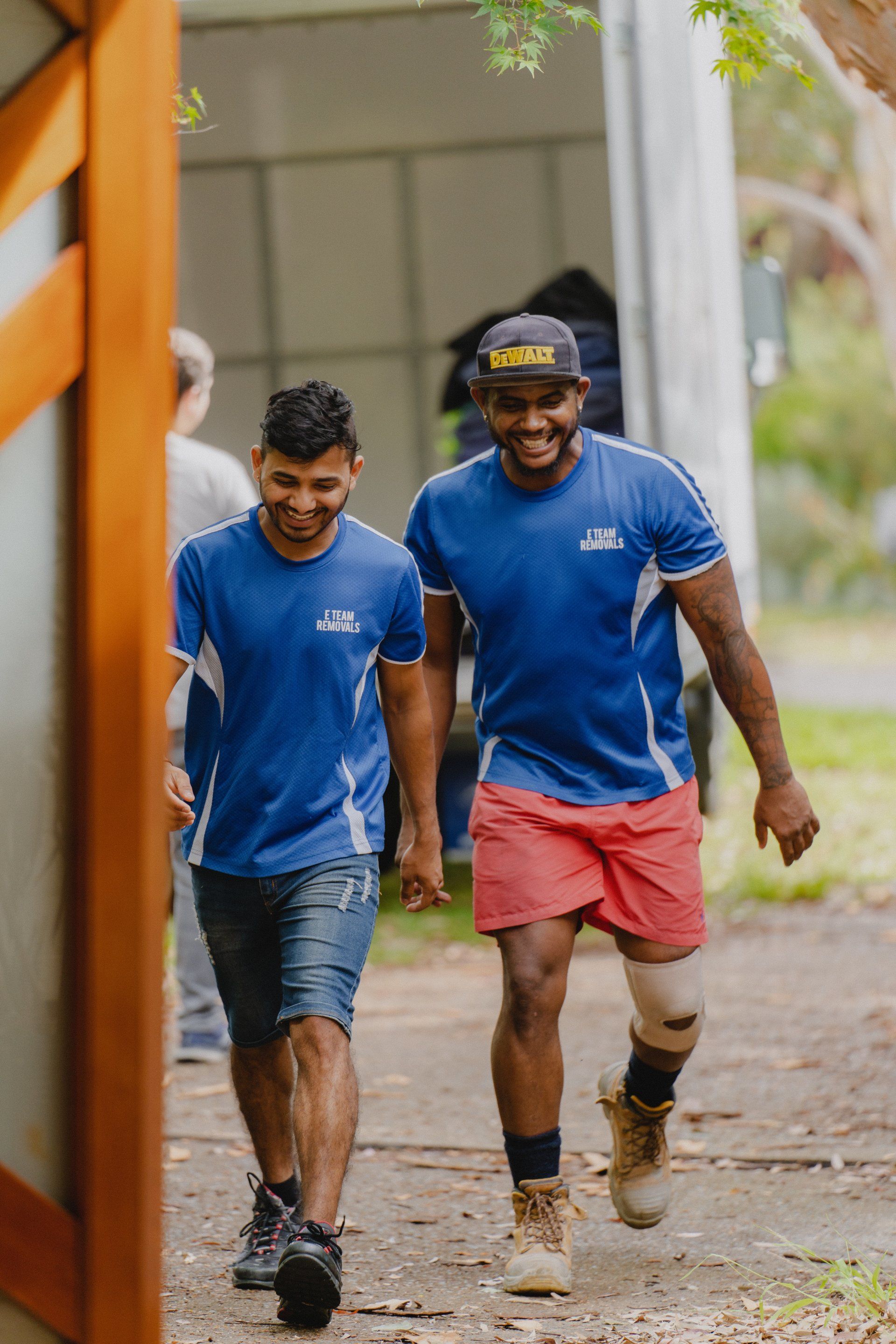 Two people in blue shirts walking outdoors on a wet path, smiling and chatting