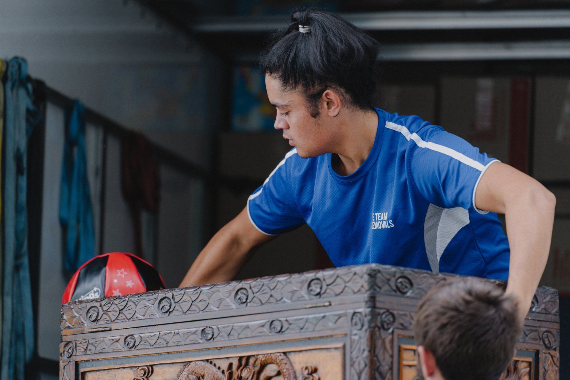 Man in blue shirt loading a carved wooden chest with a red item on top