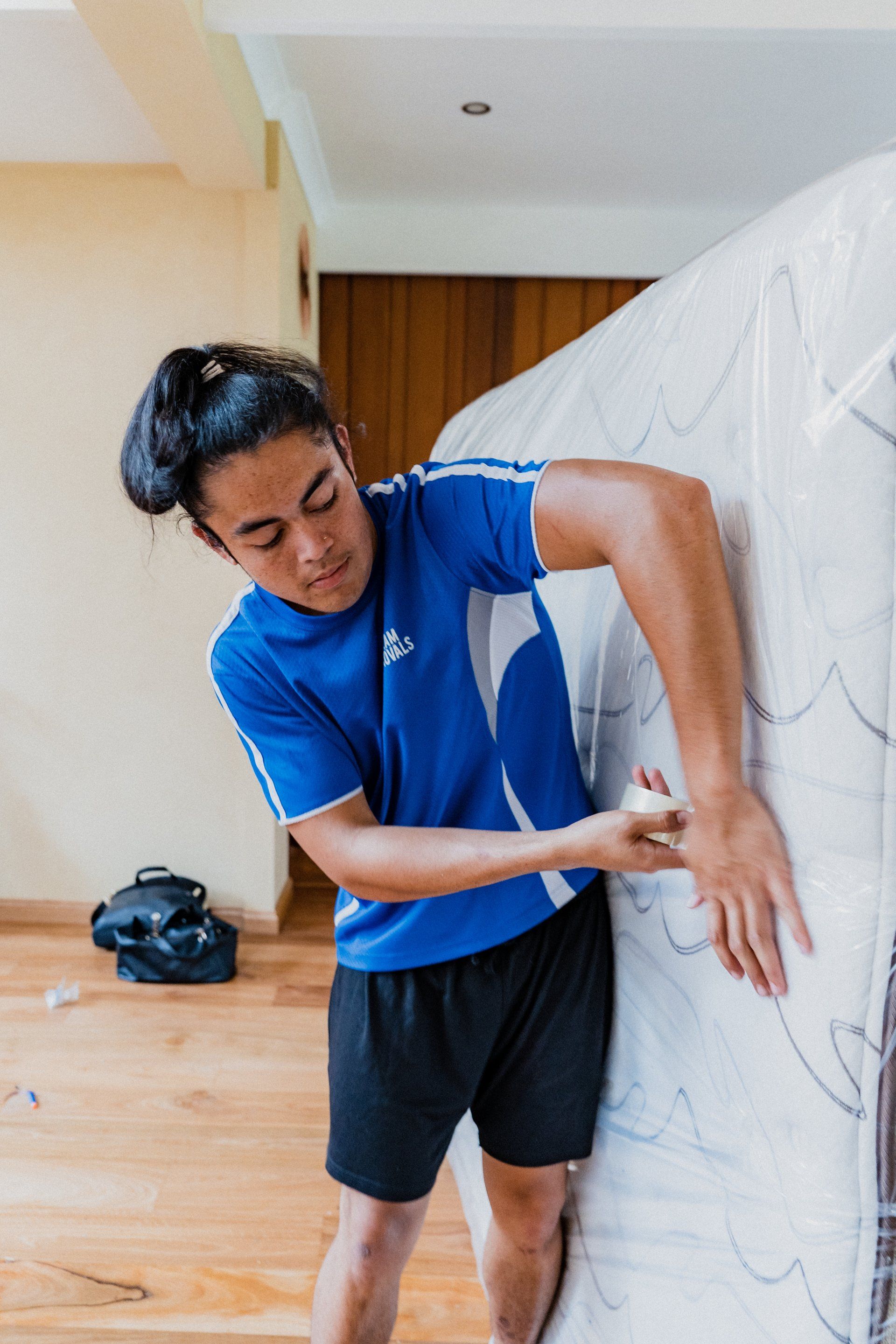 Man in blue shirt stretching beside a white padded surface in a bright indoor room