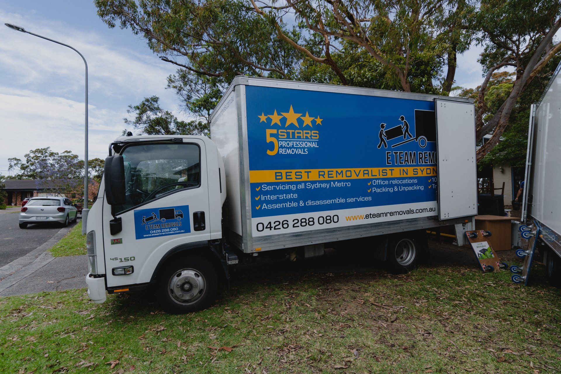 White truck with blue-and-yellow service signage parked on grass by a roadside