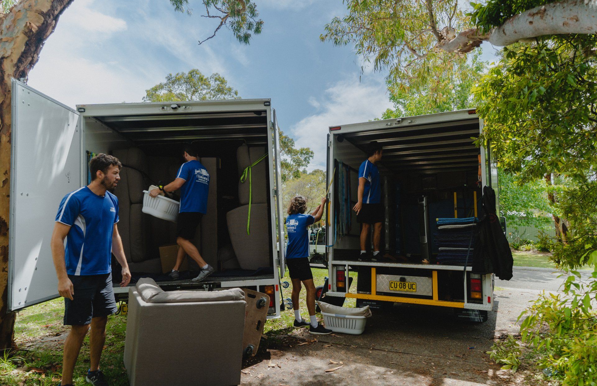 People unloading boxes from two trucks on a wooded roadside.