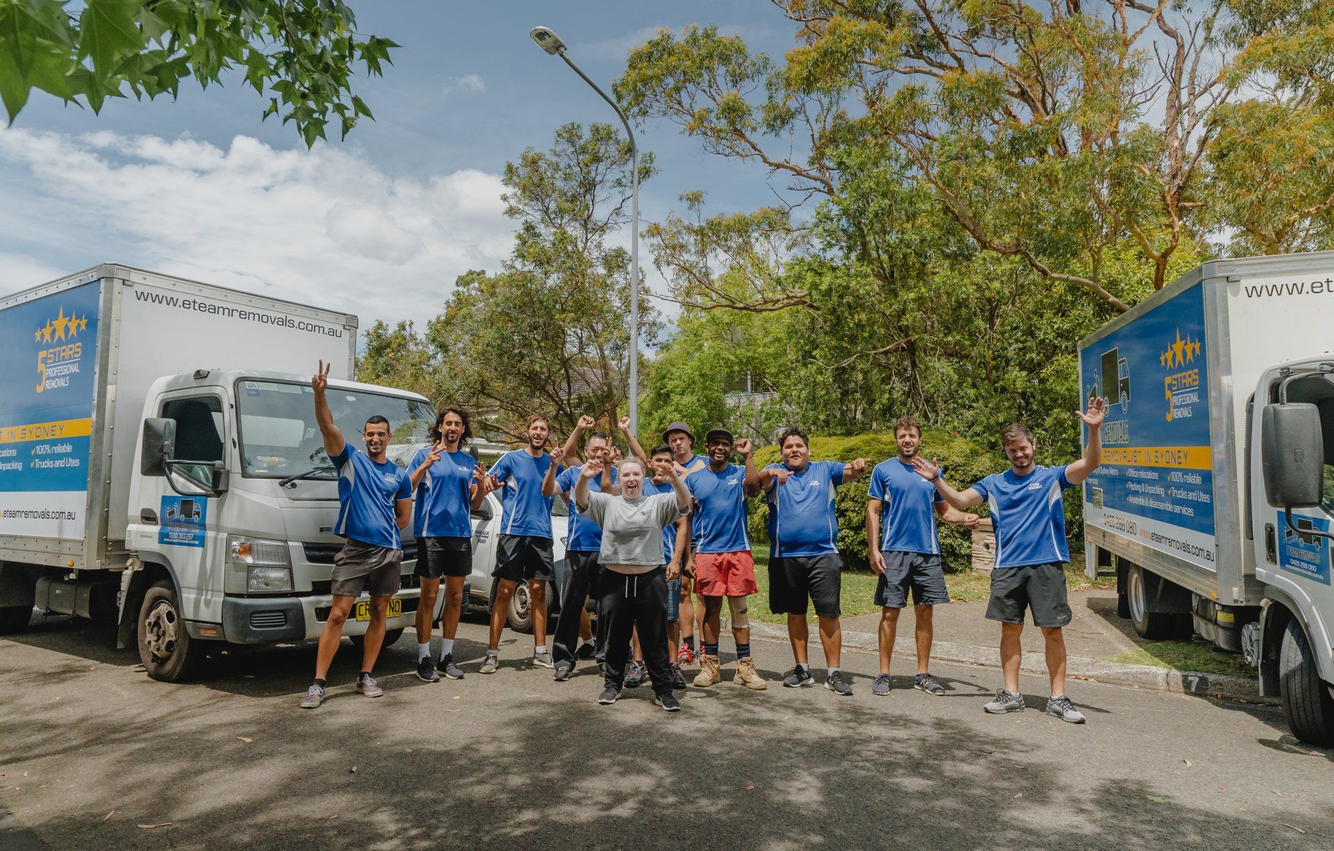 Group of volunteers in blue shirts posing between two trucks on a tree-lined road