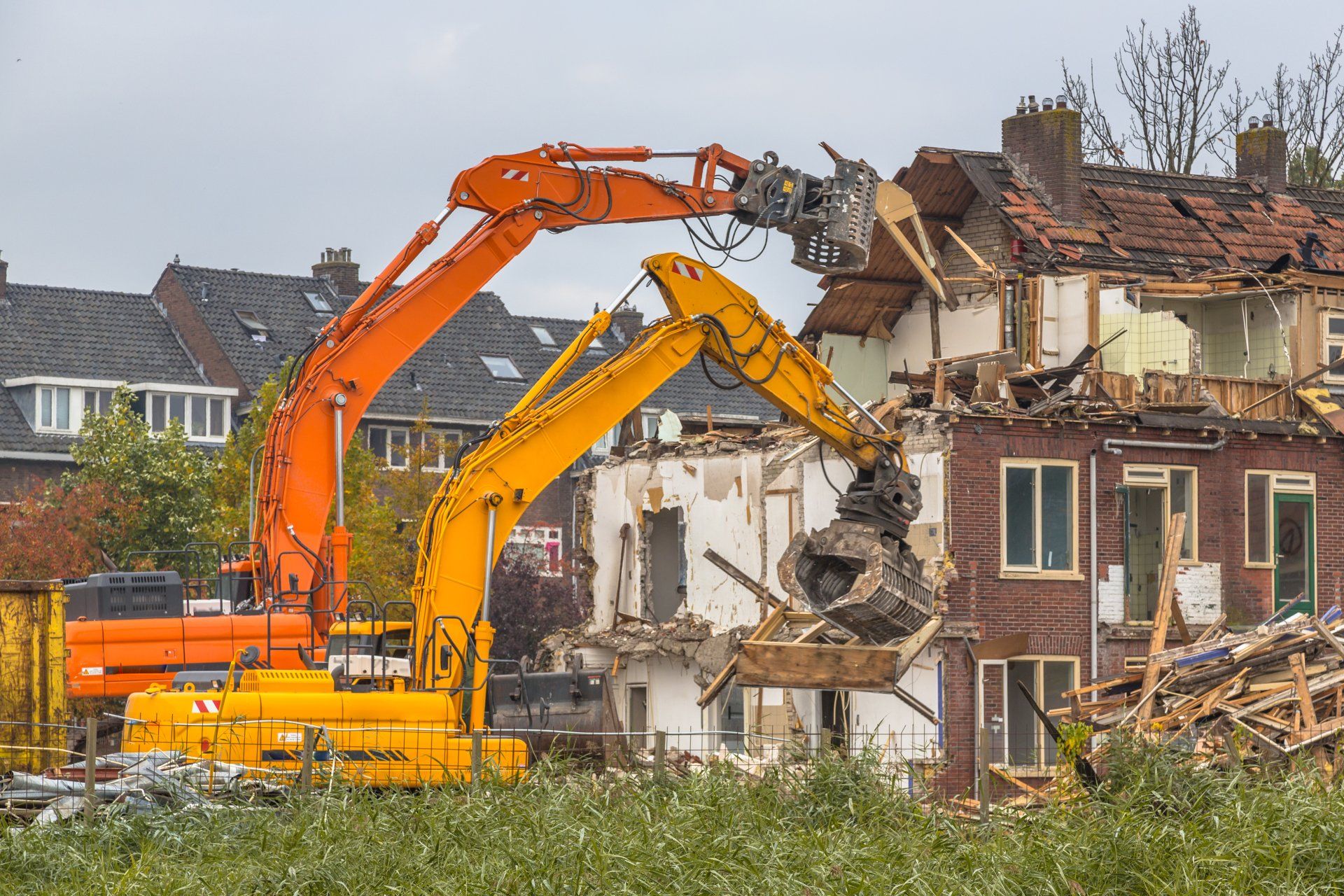 Two excavators demolishing a brick house in a residential neighborhood