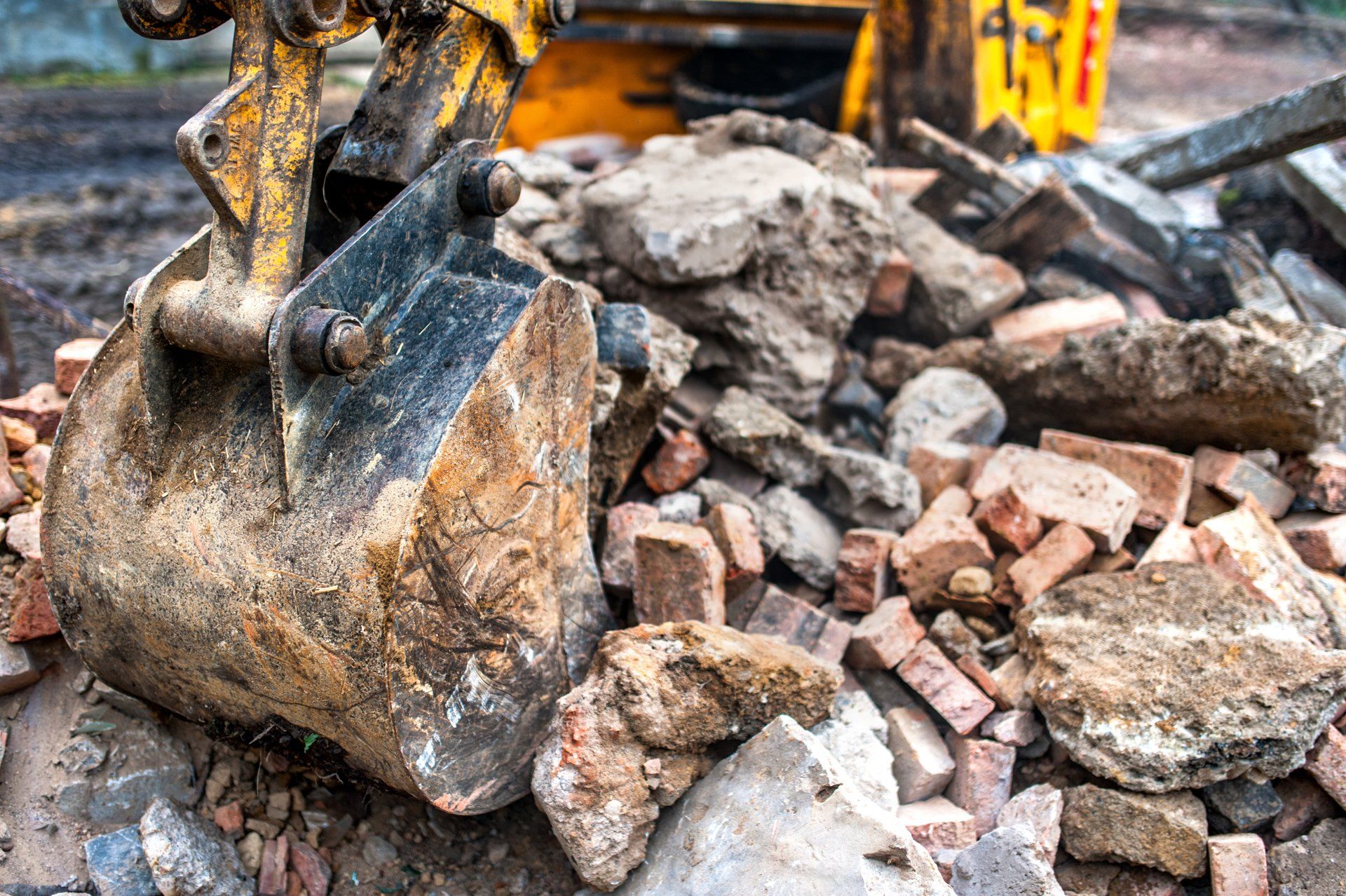 Excavator bucket digging through a pile of broken concrete and rubble at a construction site